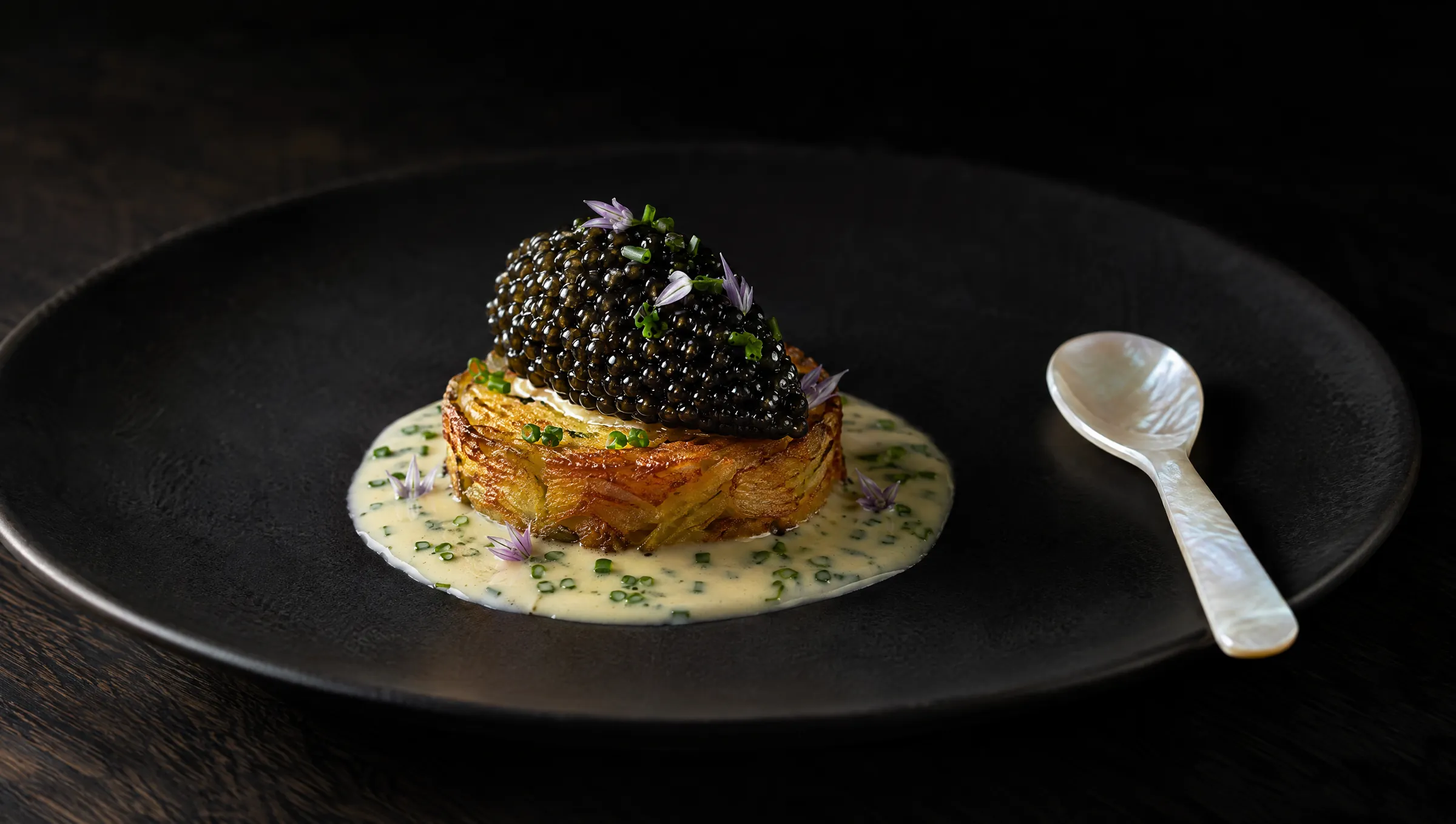 Kartoffelgalette mit Oscietra-Kaviar und Beurre blanc, daneben ein Perlmuttlöffel