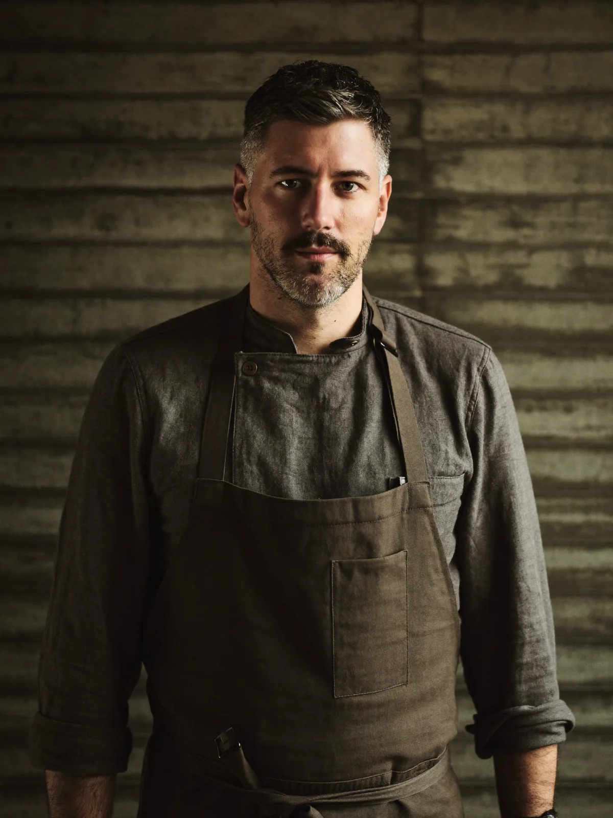 Porträt von Felix Albrecht, Küchenchef, vor einer Wand aus rohem Beton